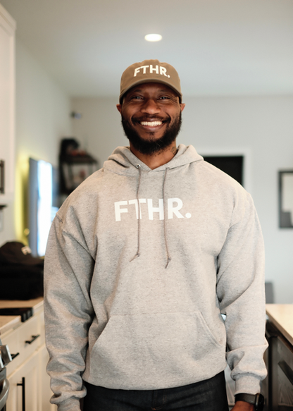 Man wearing a gray hoodie and green cap with 'FTHR.' branding indoors.