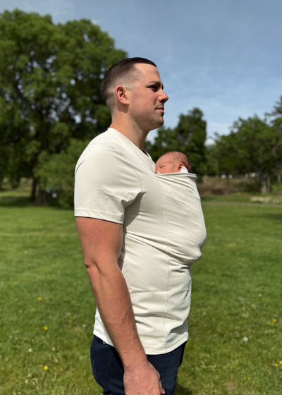 Dad wearing his baby in a Natural Dad Shirt, standing in a grassy field with trees.