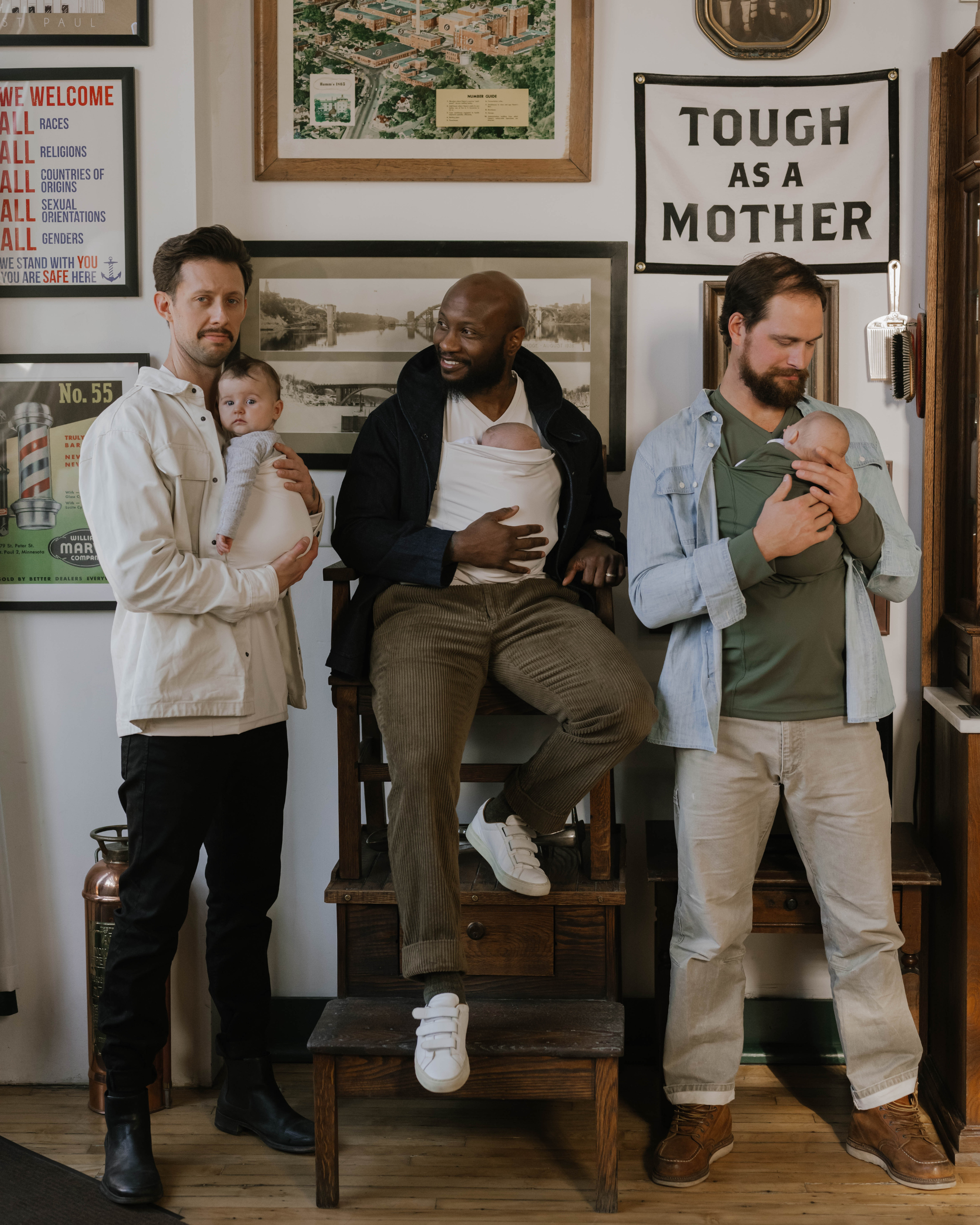 3 dads wearing their newborns in Lalabu Dad Shirts inside a barber shop.