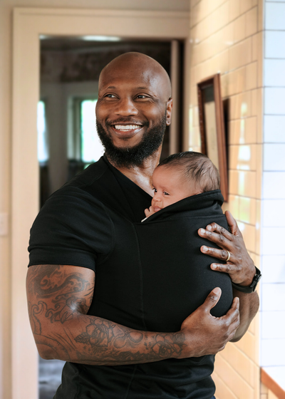 Dad wearing his baby in the pouch of his black Dad Shirt inside a house. 