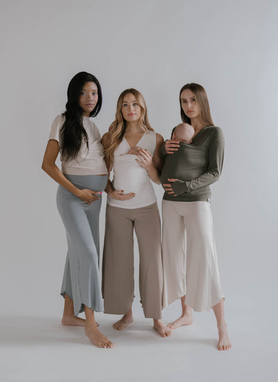 Full body view of 3 females, one is pregnant, 2 are wearing newborns in Soothe Shirts.
