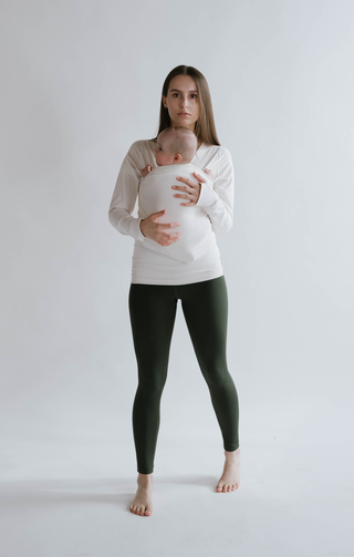 Front view of a female in green high waisted leggings with a newborn in a long sleeve Soothe Shirt.