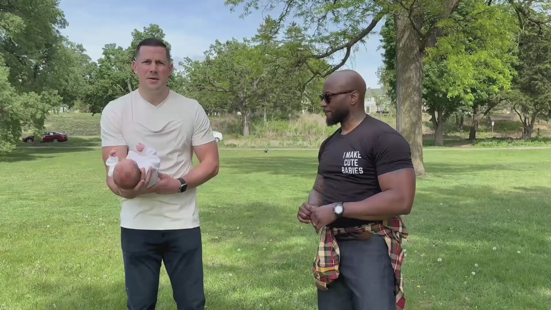Load video: 2 Dads at a park, one puts his baby into the pouch of his Natural Dad Shirt, the other embraces his child in a big hug.