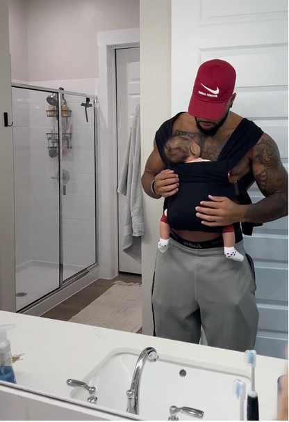 Male puts on a black Simple Wrap, puts his baby inside it and goes about his daily routine.