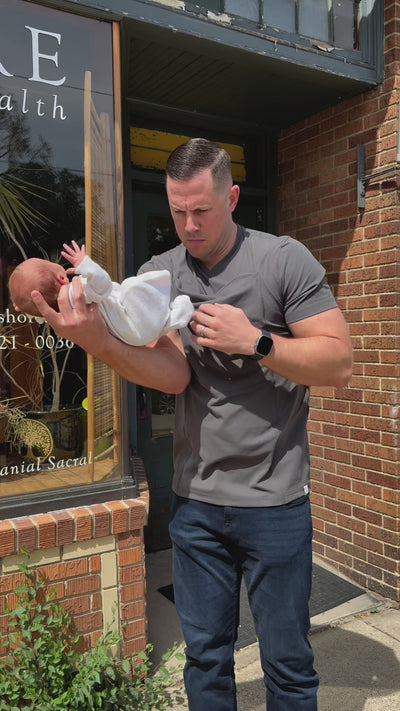 Dad pulling open the pouch of his Gray Dad Shirt and sliding his baby into it.