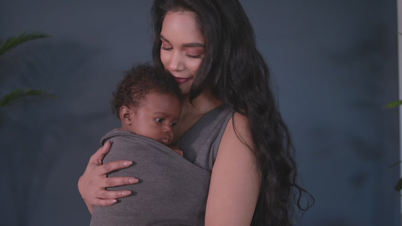 Female in a grey Soothe Shirt demonstrates how to open the pouch of the shirt, hold the newborn over her shoulder while gently lowering a newborn into it, feet first, and then gently tugging the pouch fabric up with both hands to ensure a secure fit for the baby.  The Lalabu logo is shown in white over a navy background at the end.