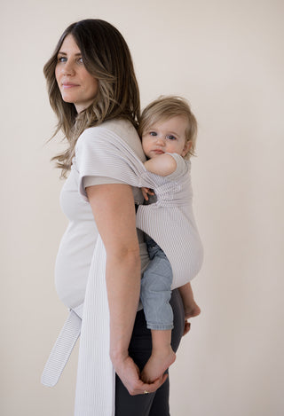 Side view of a pregnant female back carrying a baby in an Oatmeal Stripe Simple Wrap.