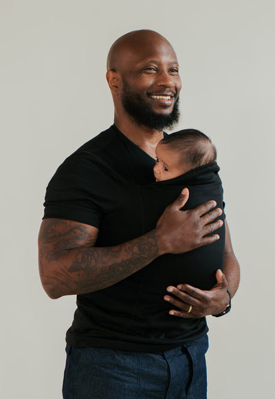 Dad smiling while wearing his baby in a black Dad Shirt.