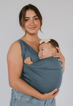 Female wearing a newborn in a Brook Soothe Shirt.