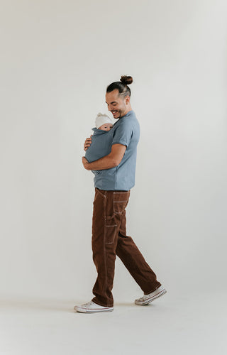 Male walking while supporting a newborn inside the pouch of a Brook Dad Shirt.
