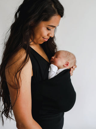 Side view of a female wearing a newborn in a black Soothe Shirt.