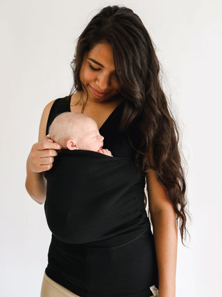 Female wearing a newborn in a black Soothe Shirt.