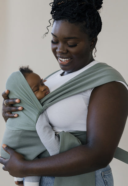Mom smiling down at the sleeping baby she's wearing in an Olive Simple Wrap.